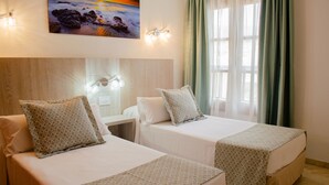 Two single beds with patterned bedding, a nightstand, a wall-mounted light fixture, and a painting of a beach scene. - Klayman Olivina Aparthotel (Arona)