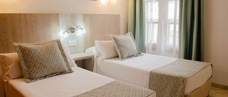 Two single beds with patterned bedding, a nightstand, a wall-mounted light fixture, and a painting of a beach scene.