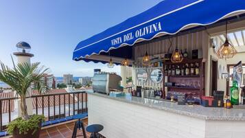 Un bar en la azotea llamado "Vista del Olivina" con toldo azul, barra y zona de estar.