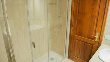 A bathroom with a glass-enclosed shower, a wooden door, and a white sink.