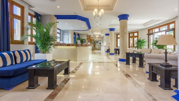 A spacious lobby with a blue sofa, a reception desk, and a chandelier. - Klayman Olivina Aparthotel (Arona)