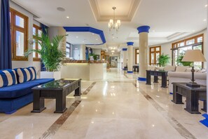 A spacious lobby with a blue sofa, a reception desk, and a chandelier. - Klayman Olivina Aparthotel (Arona)
