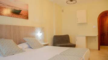 Habitación de hotel con cama, dos almohadas, una silla, mesita de noche, mueble empotrado en la pared y una puerta.