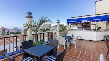 Una terraza en la azotea con mesas, sillas, una zona de bar y vistas de la ciudad.