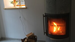 A room with a wood-burning stove, a window with a lamp, and a basket on the floor.