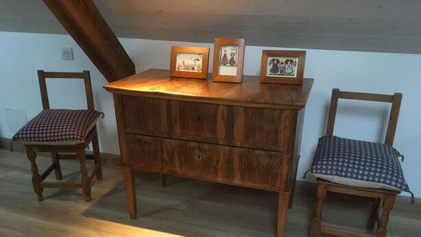A wooden dresser with three framed pictures, two wooden chairs with patterned cushions, and a sloped ceiling.