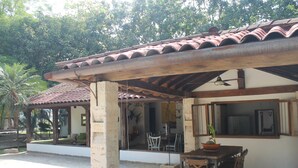 A covered outdoor dining area with a table and chairs, a ceiling fan, and a view of the interior through a glass door.