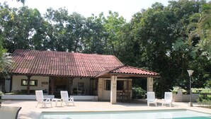 A pool area with a tiled roof structure, white lounge chairs, and a covered seating area.
