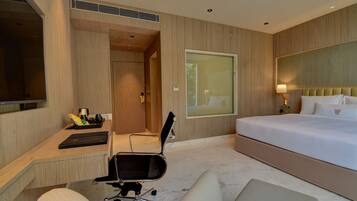 Una habitación de hotel moderna con una cama grande, un escritorio con silla, un televisor y un ventanal amplio.