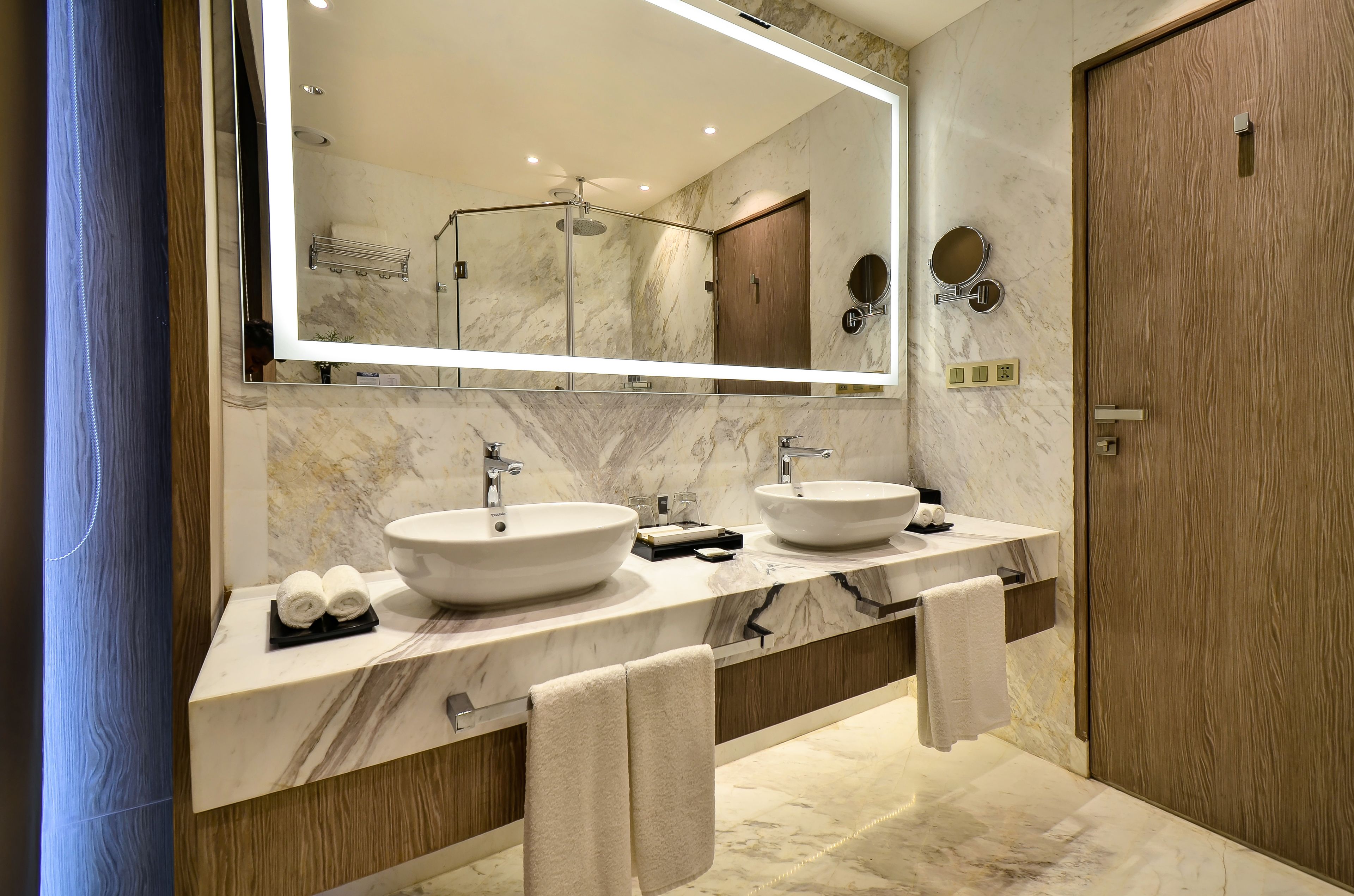 A modern bathroom with two sinks, a large mirror, and a wooden door.