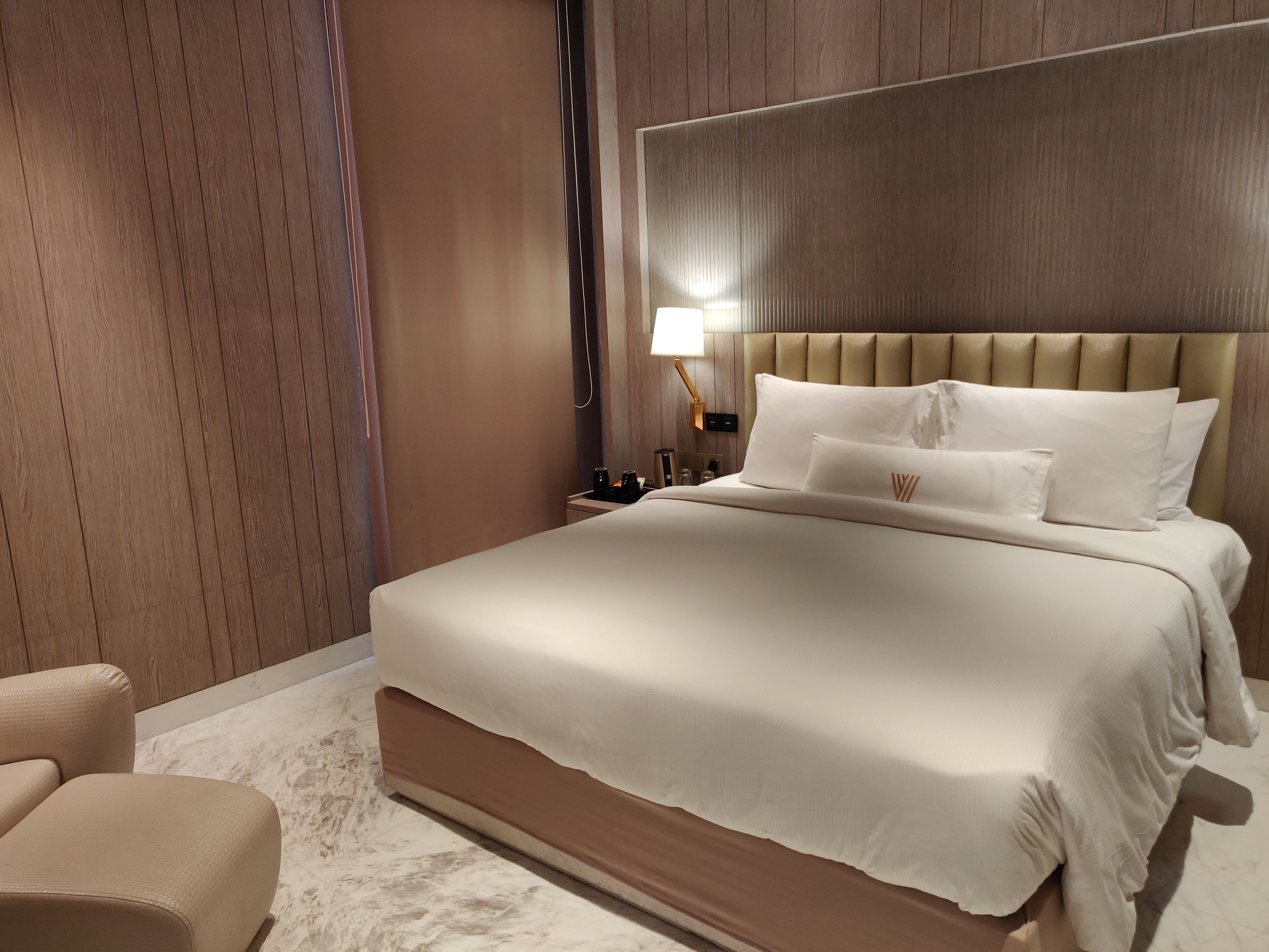 A hotel room with a large bed, a nightstand, a lamp, and a chair.