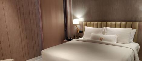 A hotel room with a large bed, a nightstand, a lamp, and a chair.