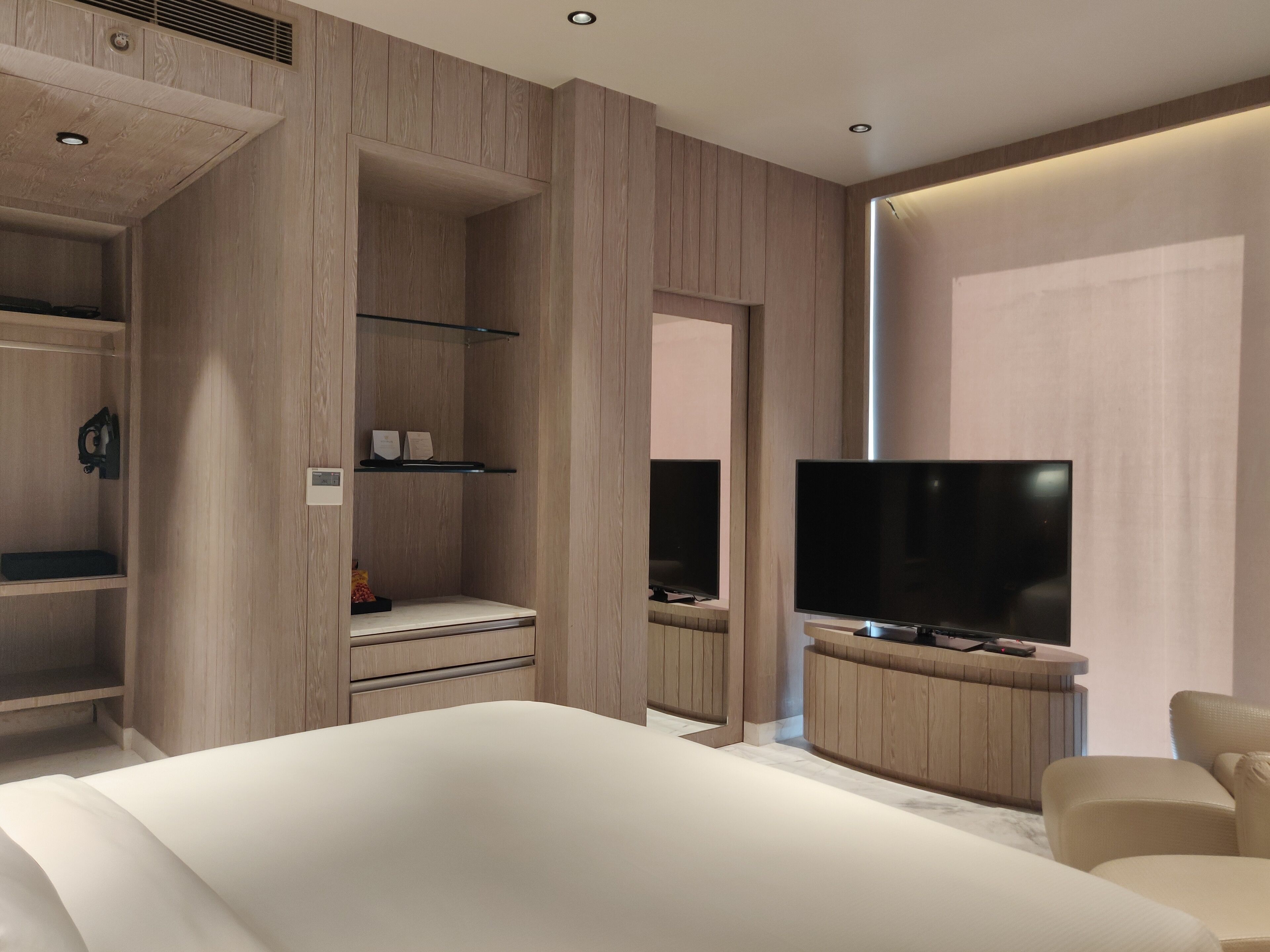 Une chambre moderne dotée d’un grand lit, d’une armoire intégrée, d’un téléviseur à écran plat et d’un coin salon avec un fauteuil.