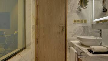A modern bathroom with a wooden door, a large mirror, a sink, and a bathtub.