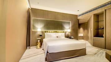 A modern hotel room with a large bed, wooden paneling, marble flooring, and built-in shelving.