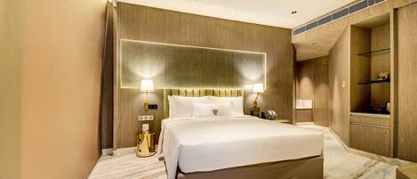 A modern hotel room with a large bed, wooden paneling, marble flooring, and built-in shelving.