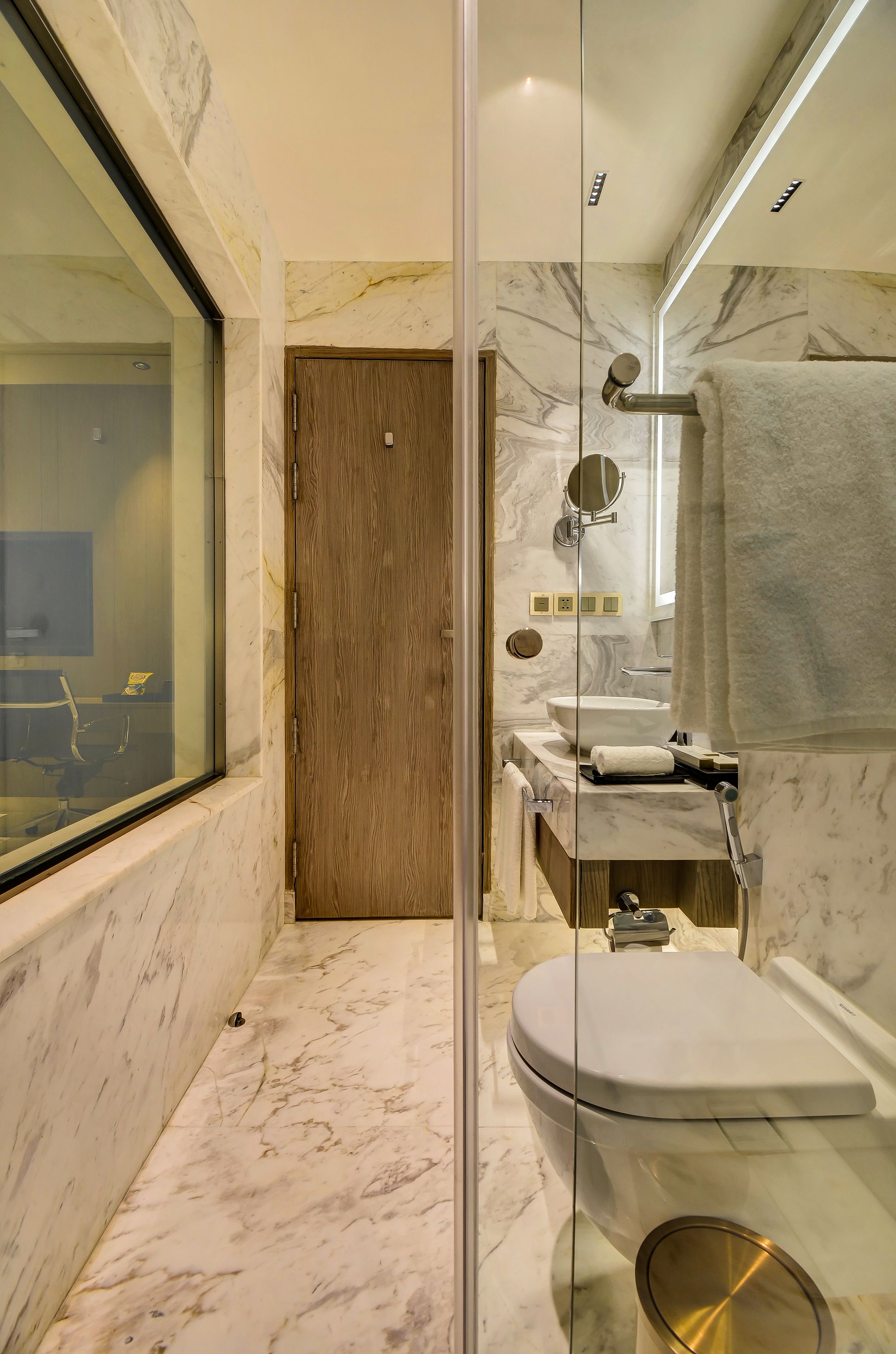 Un bany modern amb una cabina de dutxa de vidre, una porta de fusta, un vàter i un lavabo amb mirall.