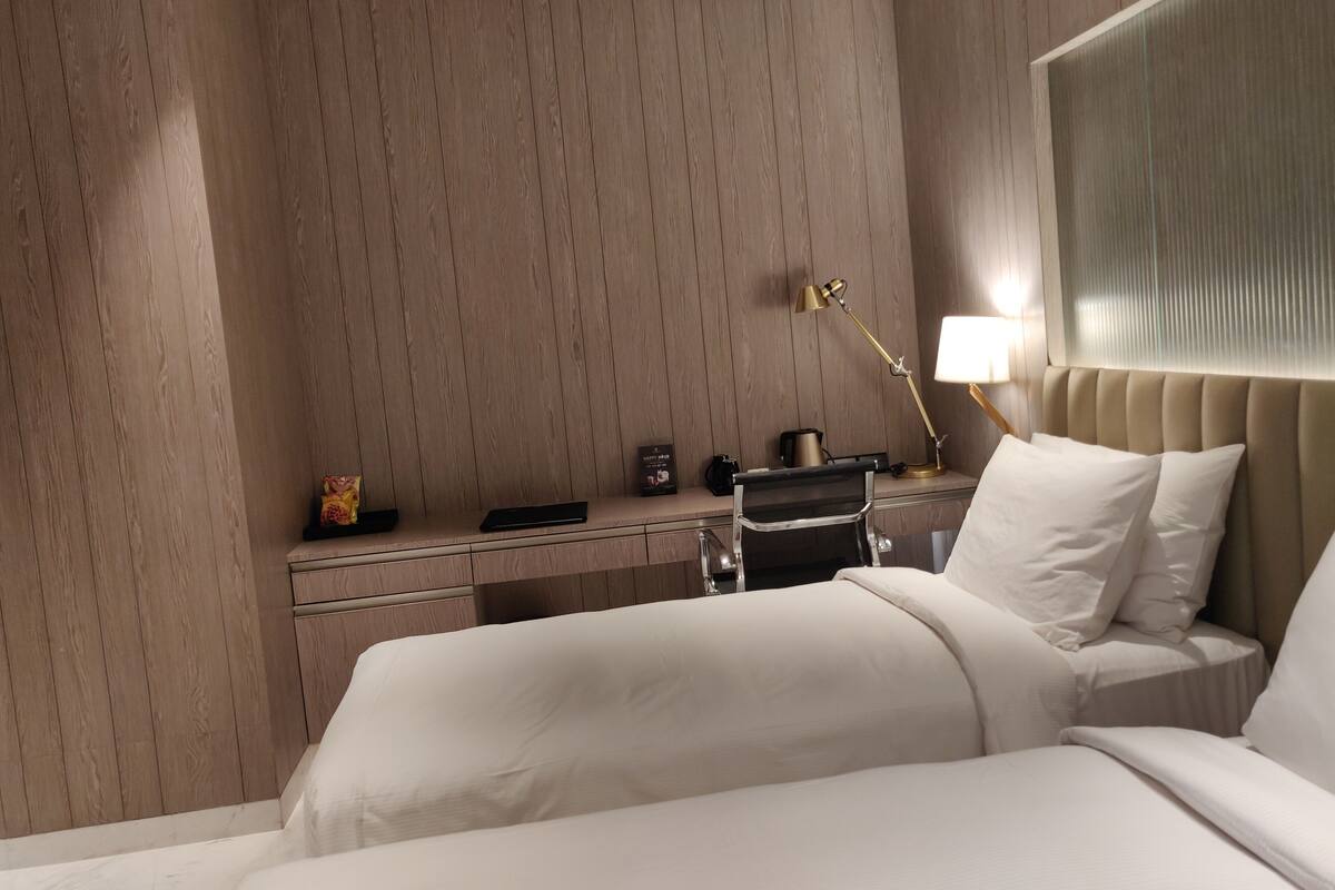 Una habitación de hotel con cama, mesita de noche, lámpara y un pequeño escritorio con silla.