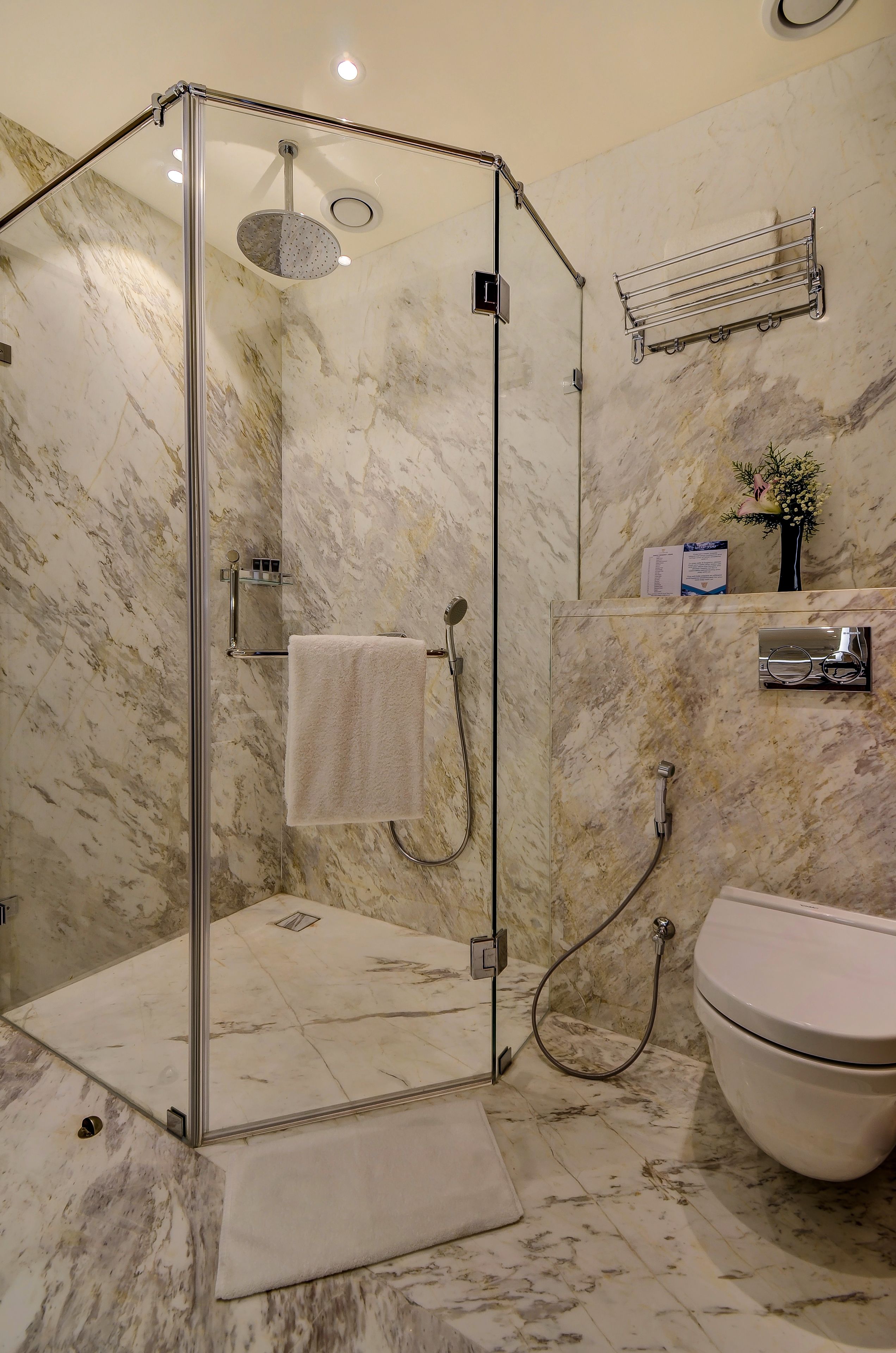 A modern bathroom with a glass-enclosed shower, marble walls, a white toilet, and a towel rack.