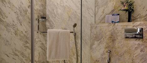 A modern bathroom with a glass-enclosed shower, marble walls, a white toilet, and a towel rack.