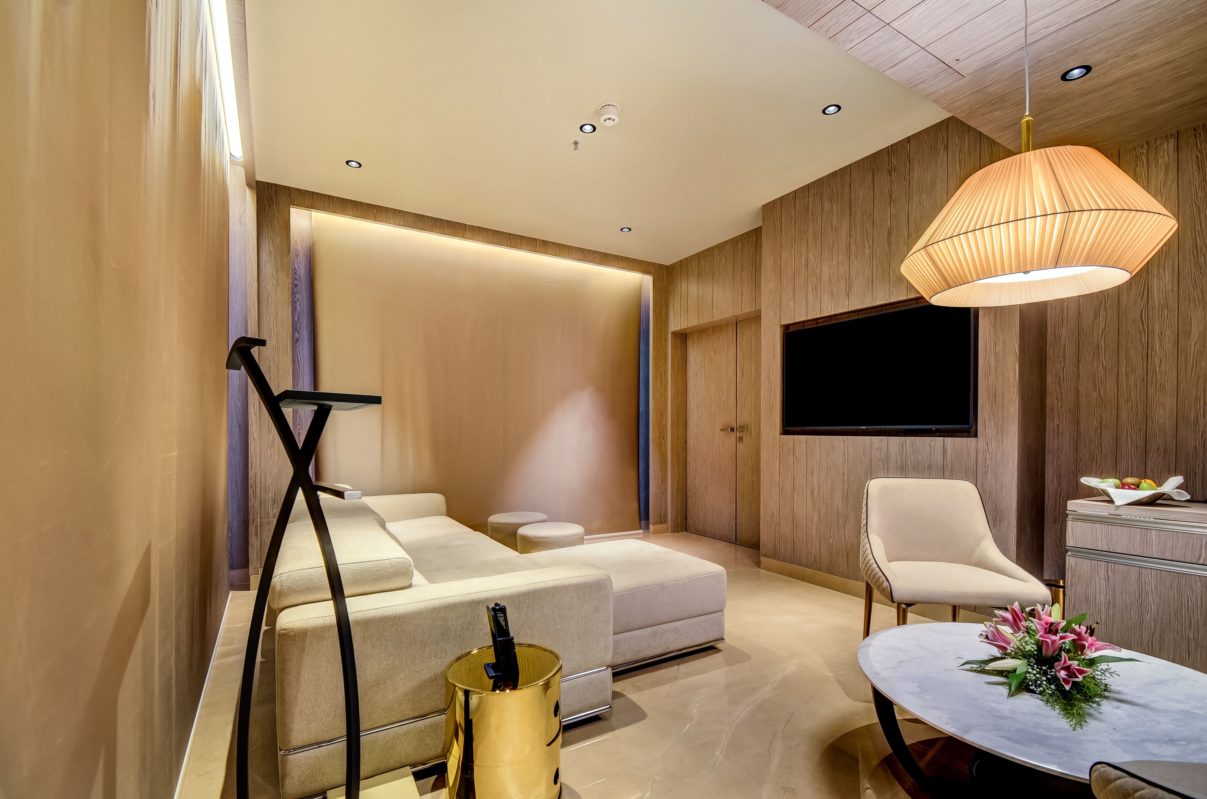 Una sala moderna con un sofá, un televisor montado en la pared, una mesa de comedor y un arreglo floral, además de una lámpara.