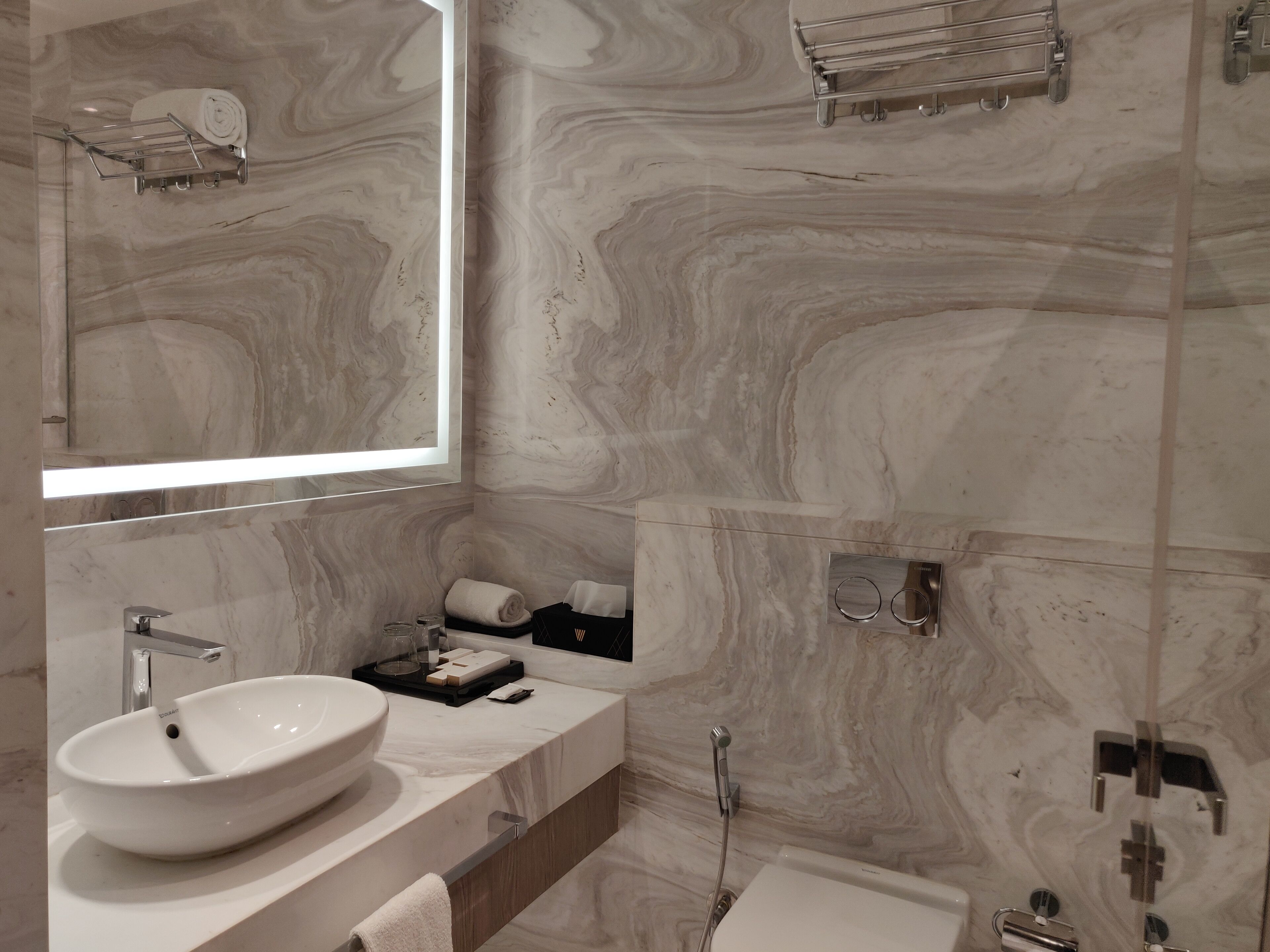 A modern bathroom with a large mirror, a white sink, a shower, and a towel rack.