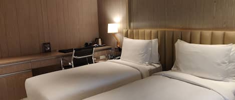 A hotel room with two beds, a desk with a chair, a lamp, and a nightstand.