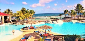 A resort pool area with lounge chairs, palm trees, and a view of the ocean. - Touba Manga Beach (Saint-François)