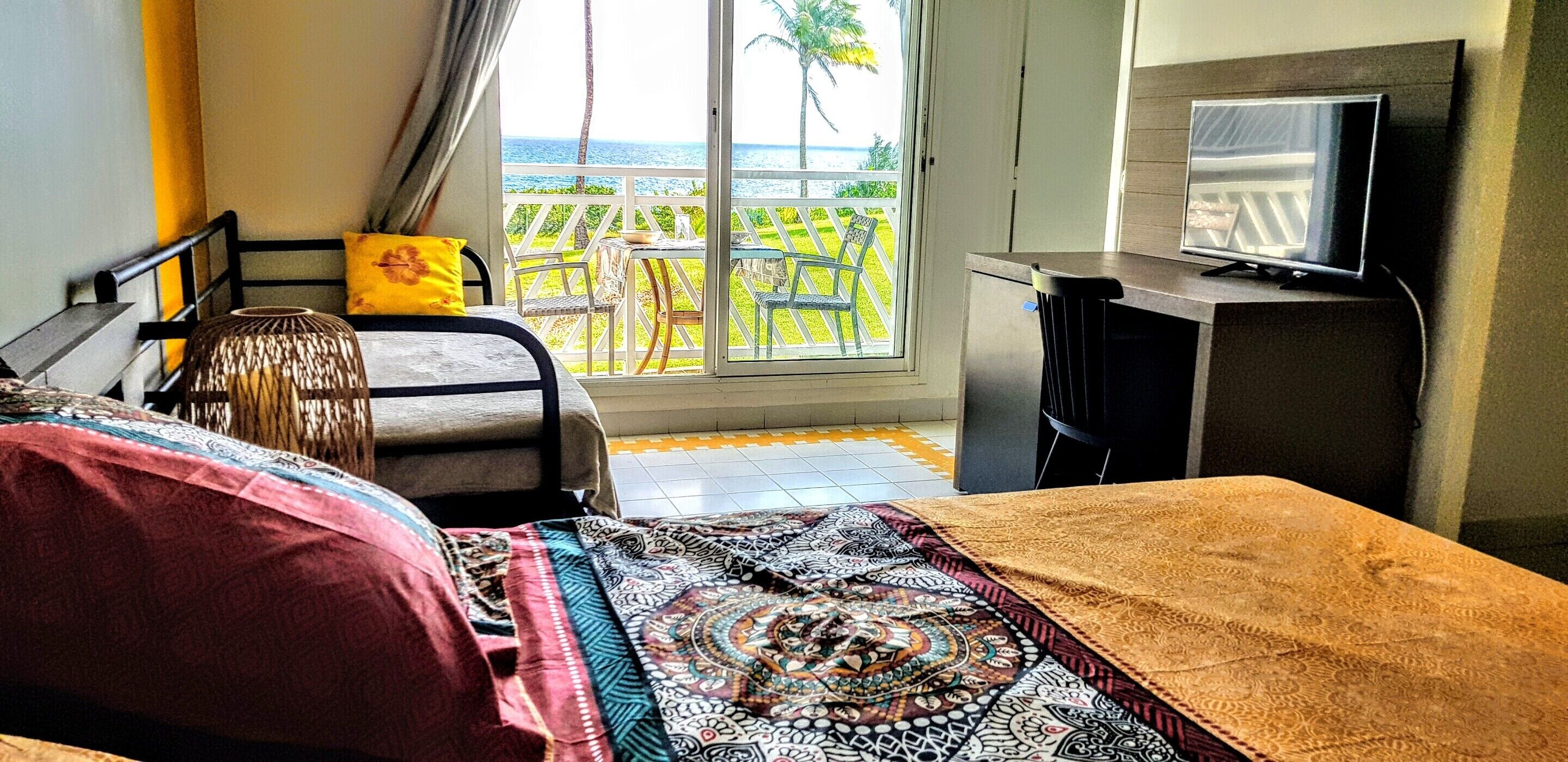 A hotel room with a bed, a television, a small table, and a view of the ocean.