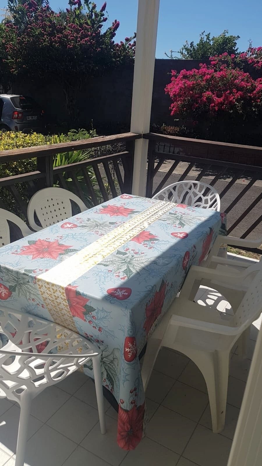 Eine Außenpatio mit einem Tisch, bedeckt mit einer blumigen Tischdecke, umgeben von weißen Plastikstühlen.