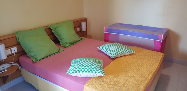 A bed with a pink mattress, green and white patterned pillows, and a yellow blanket. - Touba Manga Beach (Saint-François)