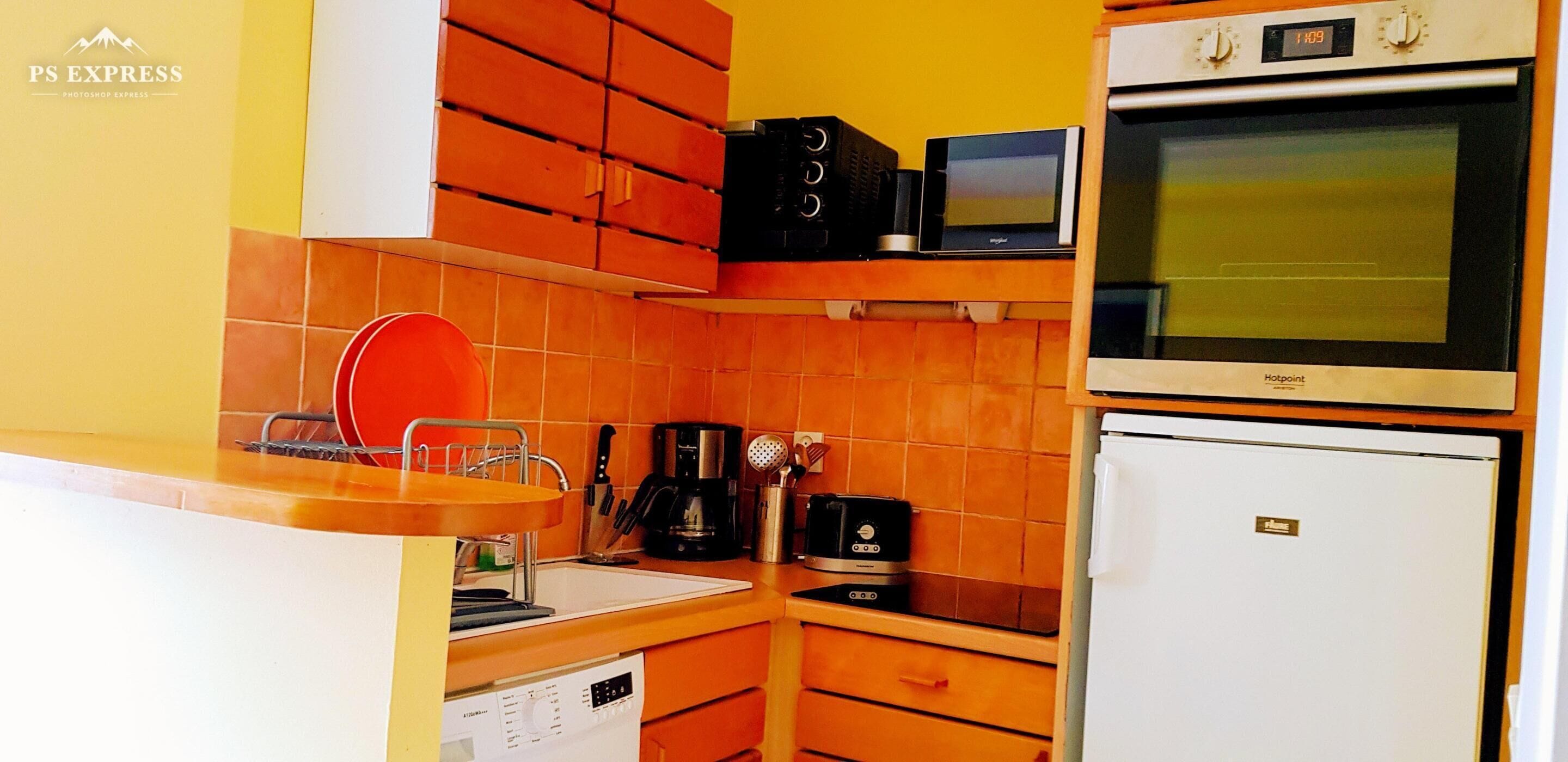 Een compacte keuken met oranje kastjes, een magnetron, een koffiezetapparaat en een koelkast.