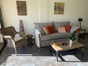 Un salon avec un canapé gris, un fauteuil en osier et une table basse.