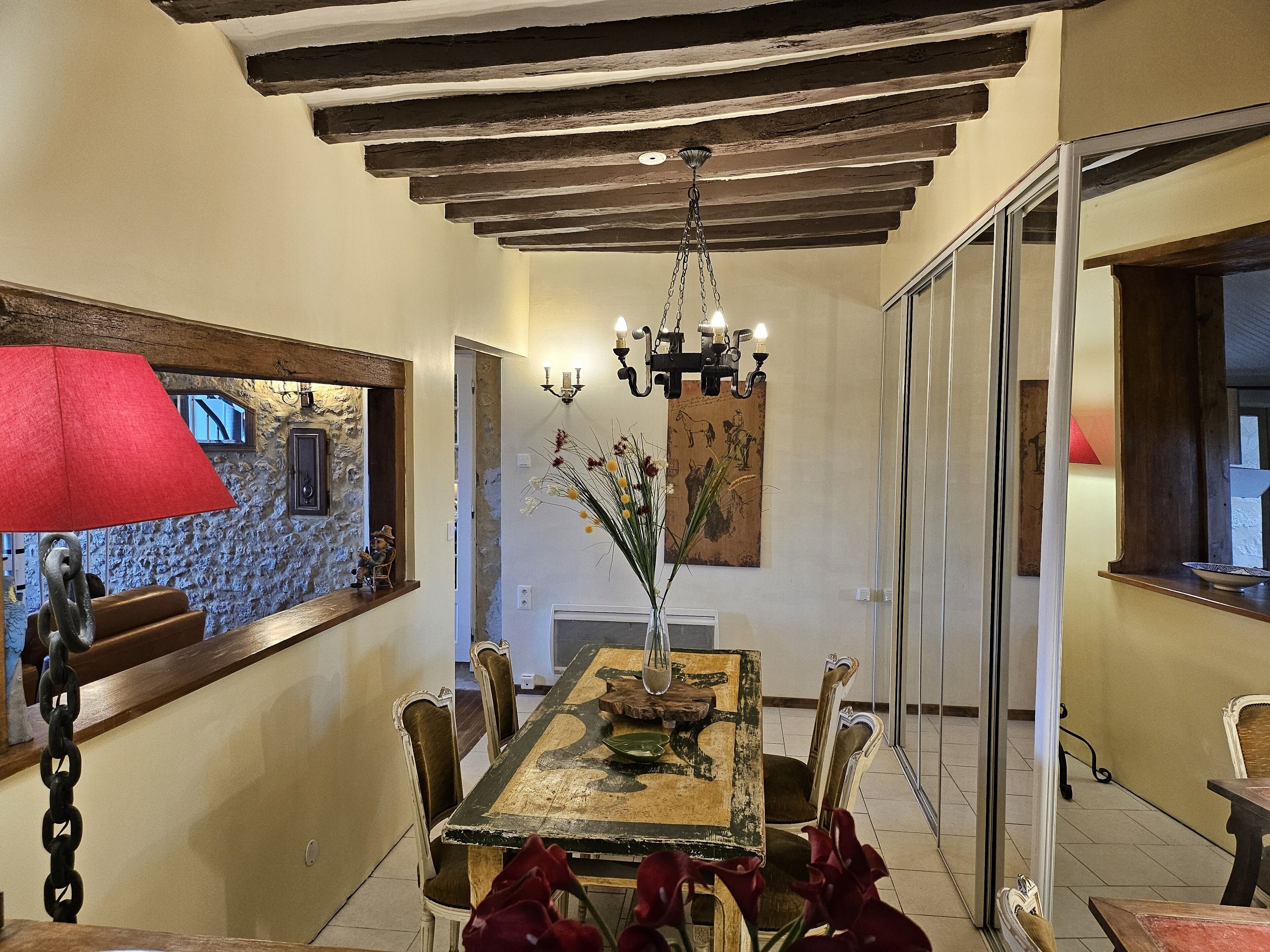 Un coin repas avec une table en bois, des chaises, un lustre et une lampe rouge.