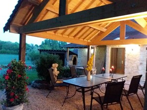Patio esterno con tavolo e sedie, circondato da muri in pietra e un pergolato in legno.
