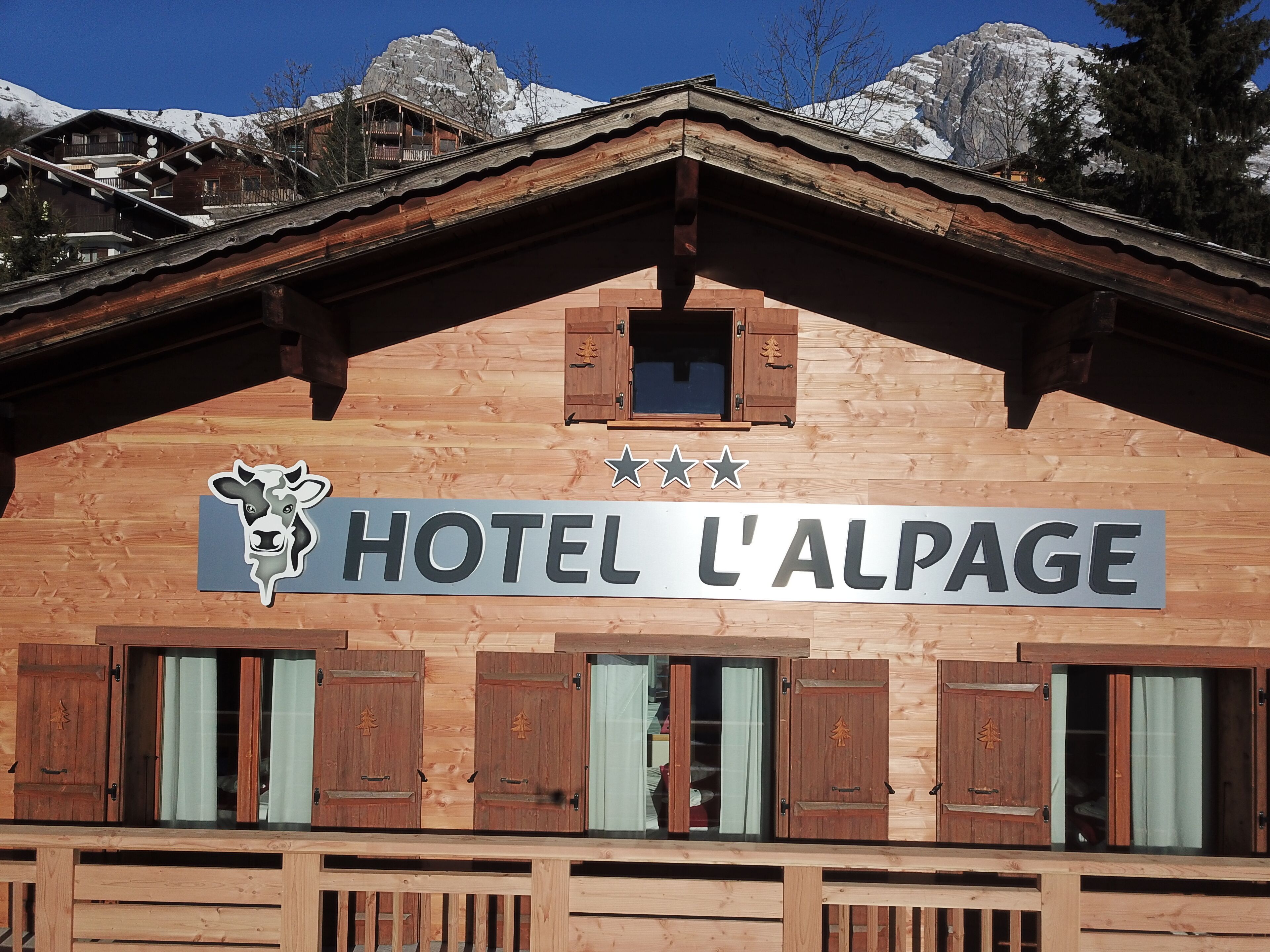 A wooden building with a sign reading "HOTEL L'ALPAGE" and a cow logo.
