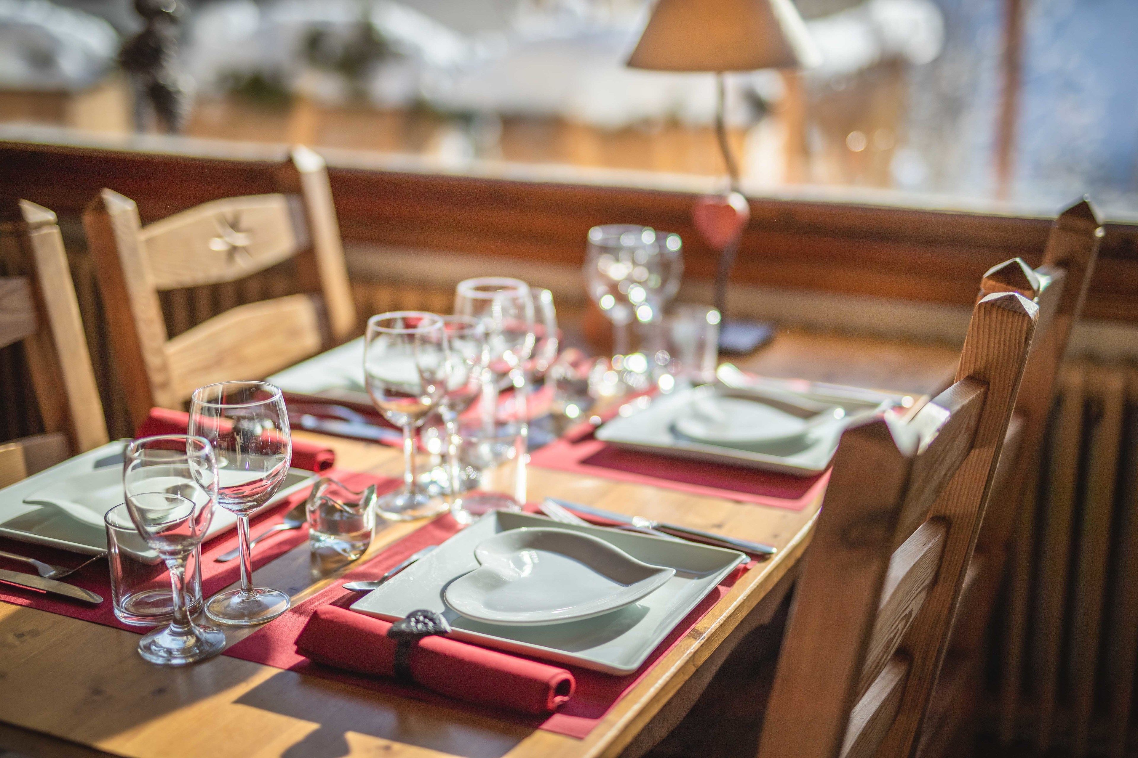 A dining table set with plates, glasses, and cutlery, with wooden chairs around it.