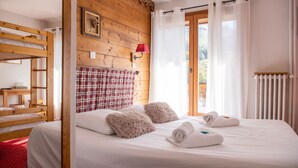 Une chambre avec un lit superposé en bois, un lit simple avec du linge de lit blanc, des oreillers moelleux et des serviettes enroulées.