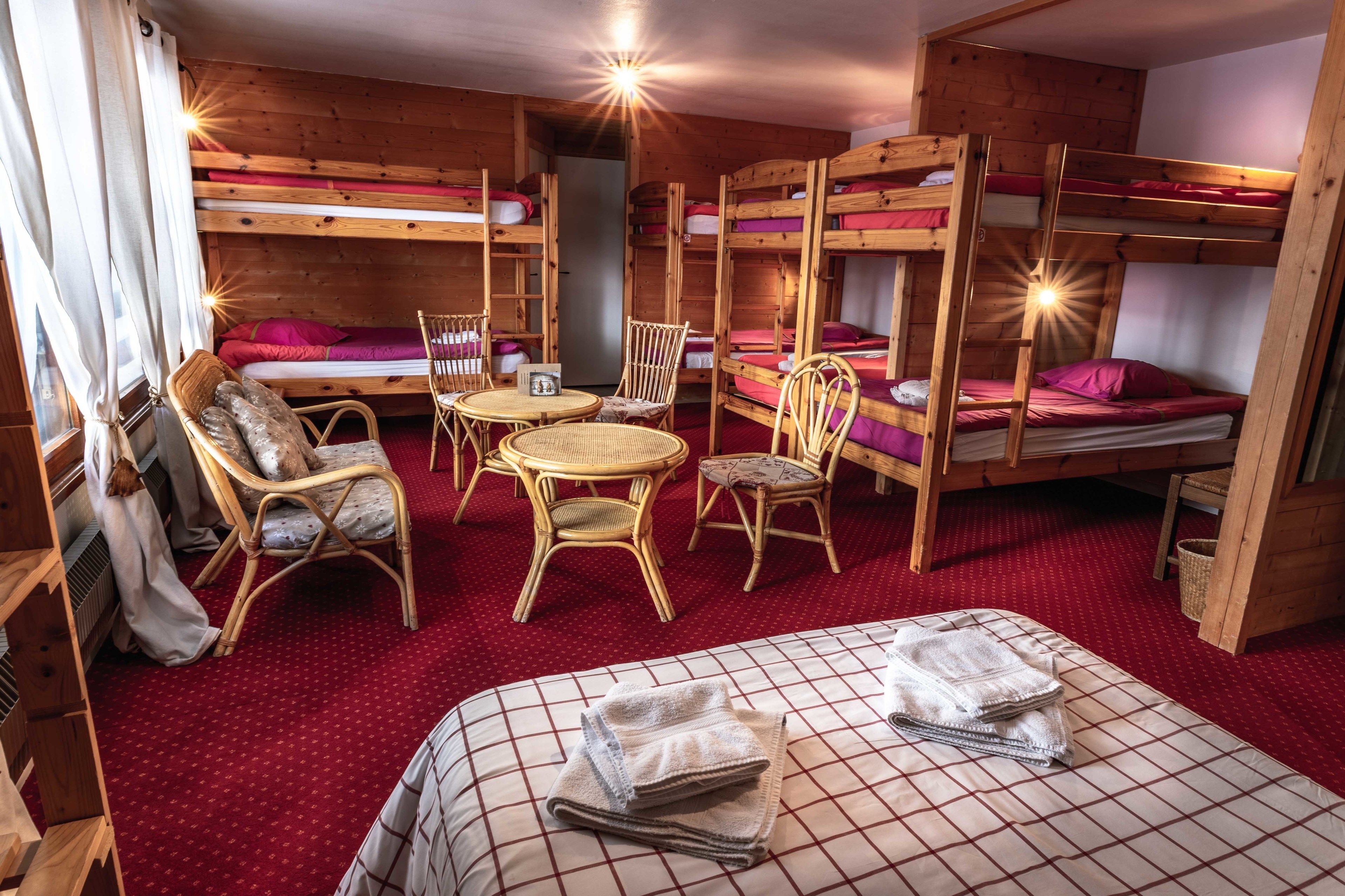 Habitación tipo dormitorio con literas, una mesa redonda, sillas de mimbre y una alfombra roja.