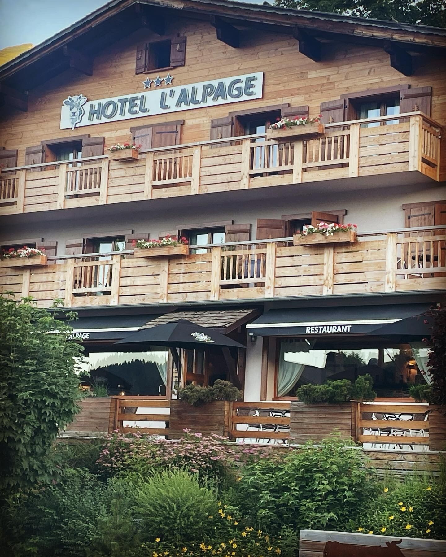 Un immeuble en bois à plusieurs étages, doté de balcons, d’un restaurant et d’une enseigne indiquant « HÔTEL L’ALPAGE ».