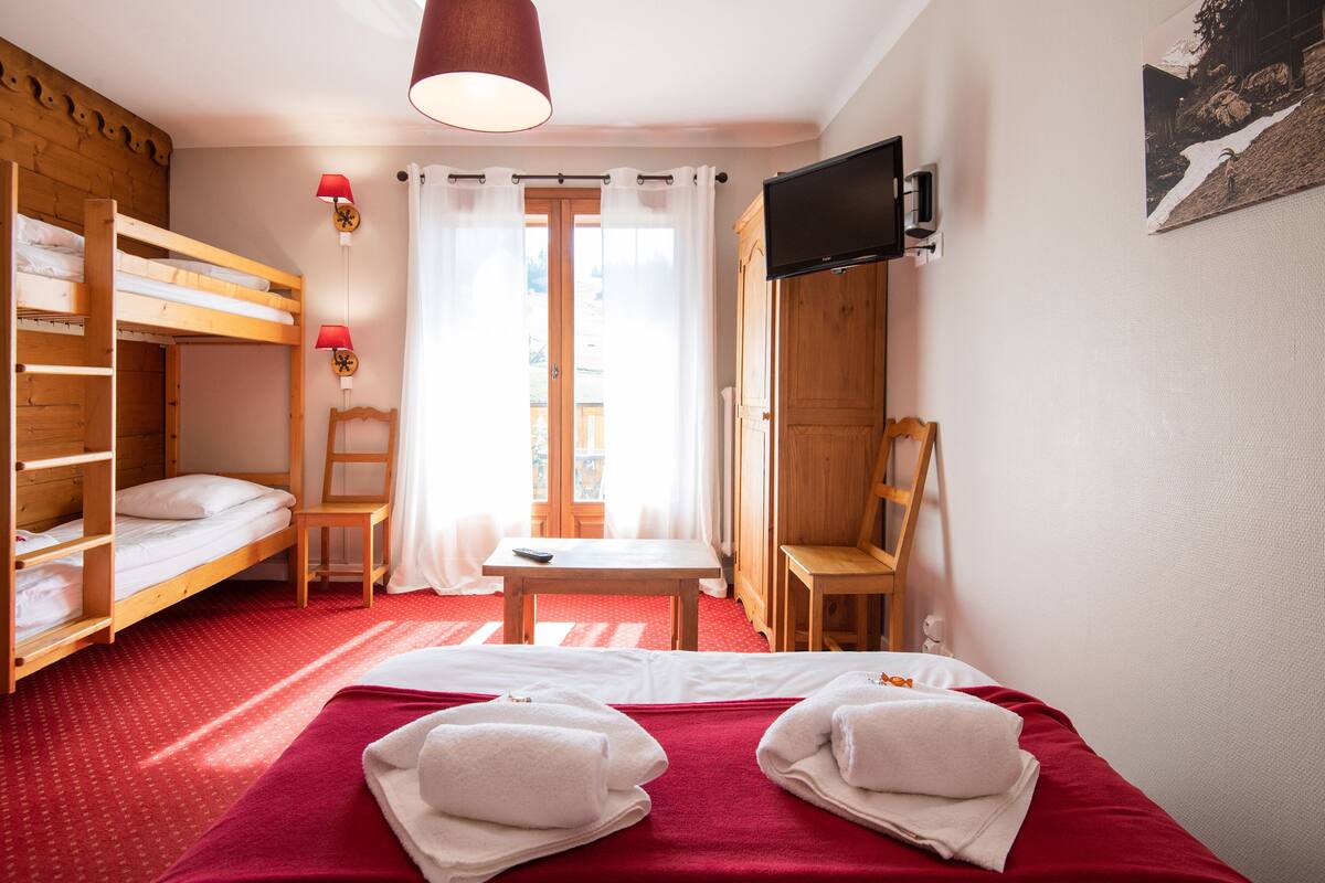 A room with bunk beds, a desk, chairs, a TV, and a window with curtains.