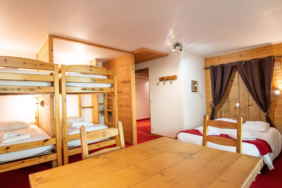 A room with bunk beds, a wooden table, and a red carpet.