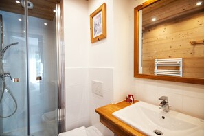 A bathroom with a glass shower enclosure, a wooden vanity with a sink, and a mirror above the sink. - Hôtel L'Alpage (Le Grand-Bornand)