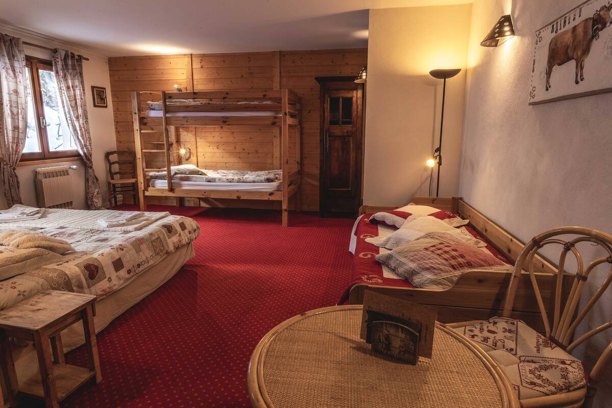 A cozy room with two bunk beds, a wooden wardrobe, a chair, a small table, and a lamp.
