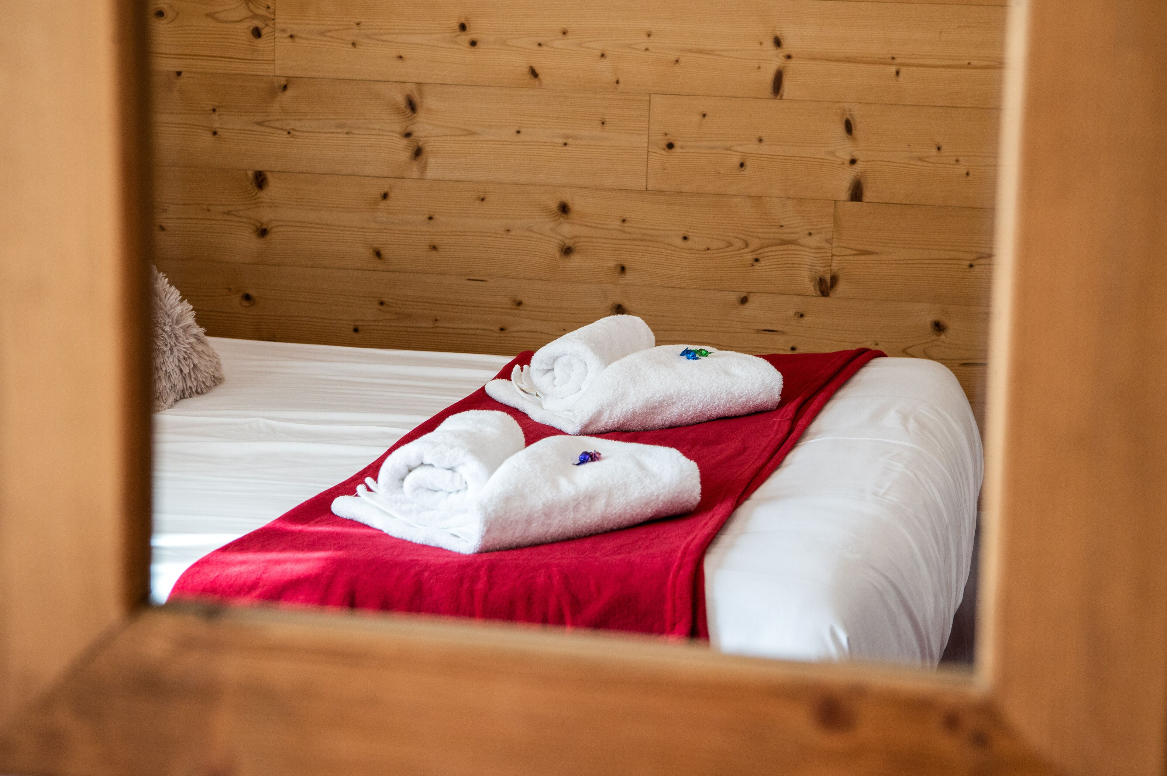 Una cama bien hecha con sábanas blancas y una manta roja, un cabecero de madera y un cojín mullido.