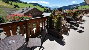 Une terrasse avec des sièges extérieurs, une vue sur un paysage montagneux et un bâtiment avec une enseigne.