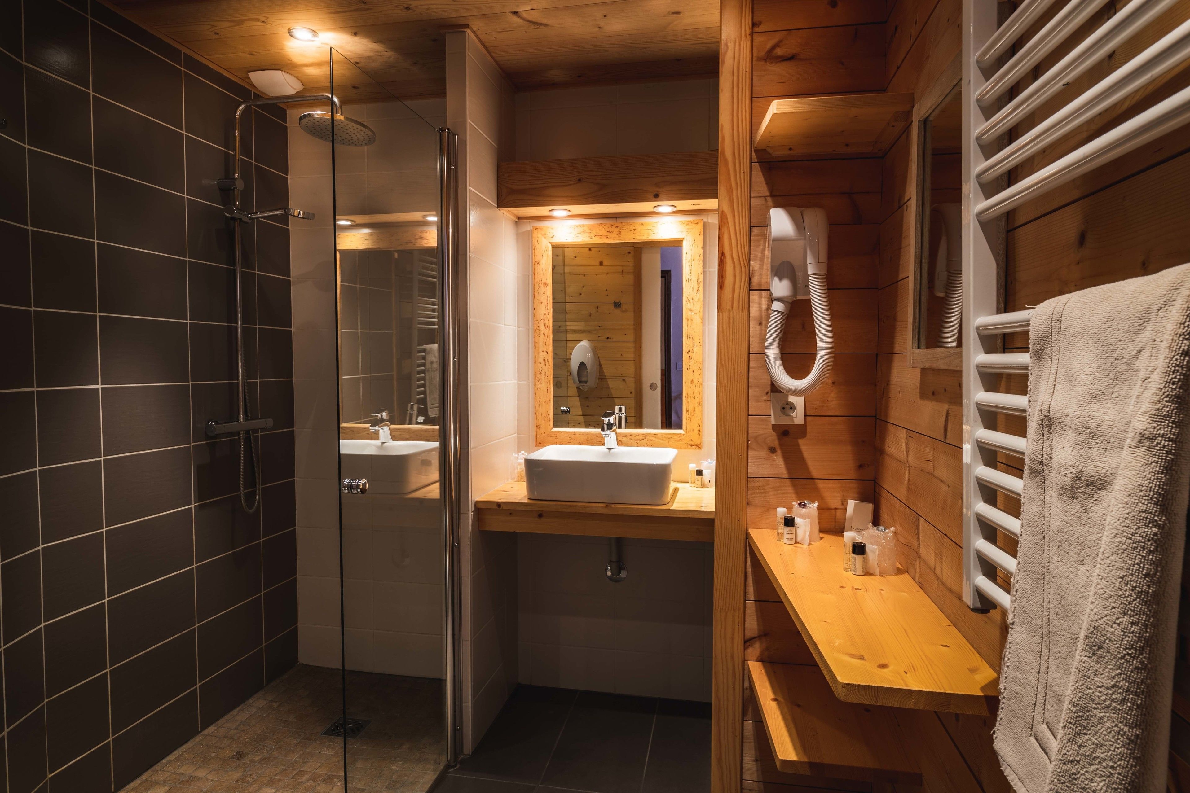 Uma casa de banho moderna com chuveiro envolto em vidro, toucador de madeira com lavatório e um porta-toalhas.