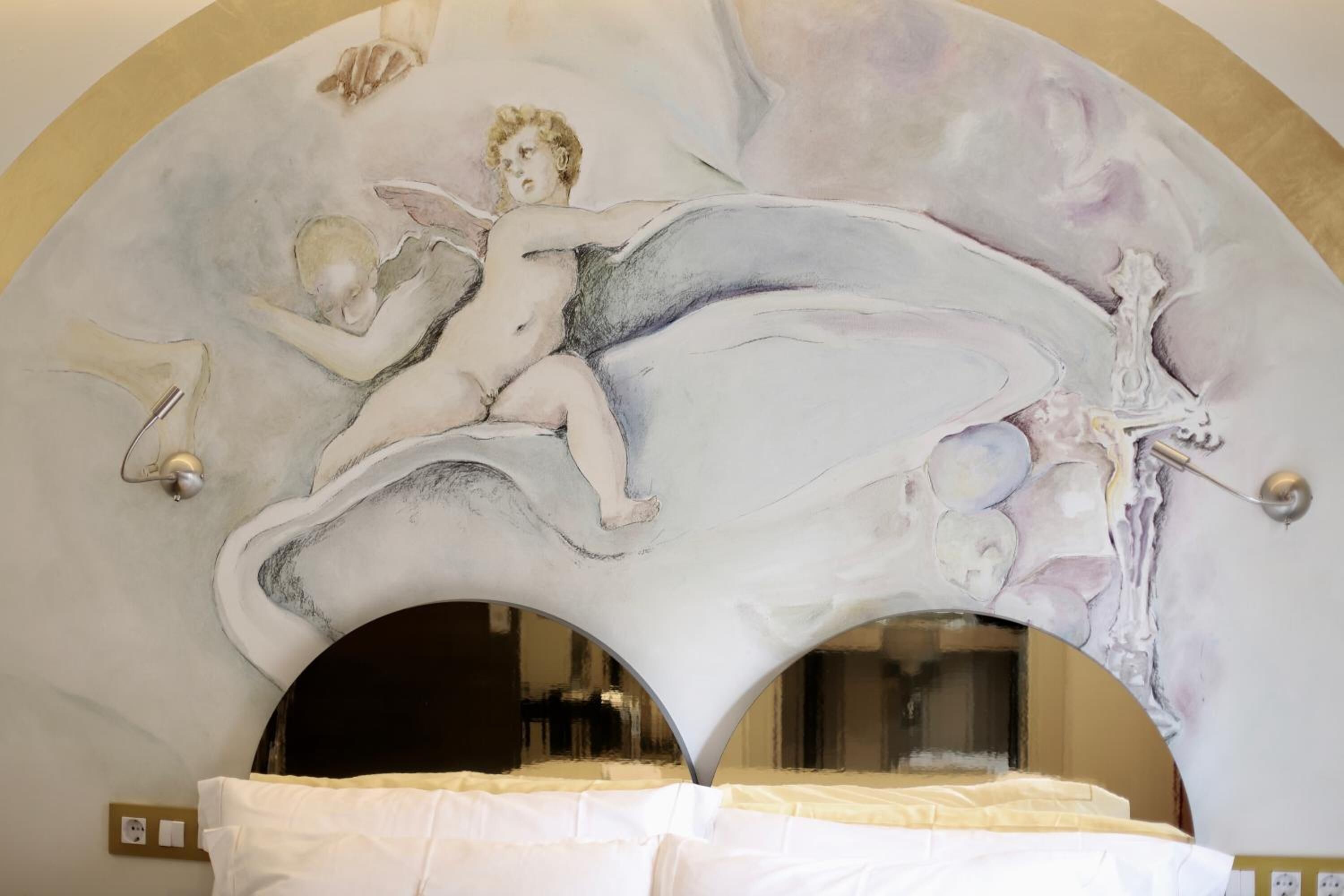 A room with a bed under a large, ornate ceiling mural depicting a winged figure.