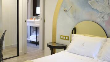 A hotel room with a bed, a bedside table, a mirror, and a wall with a painting.