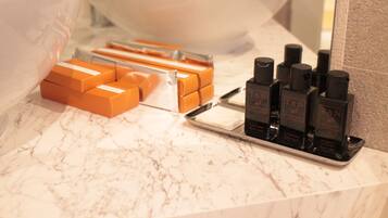 A bathroom counter with a marble surface, a large white basin, and several orange boxes and black bottles of skincare products.